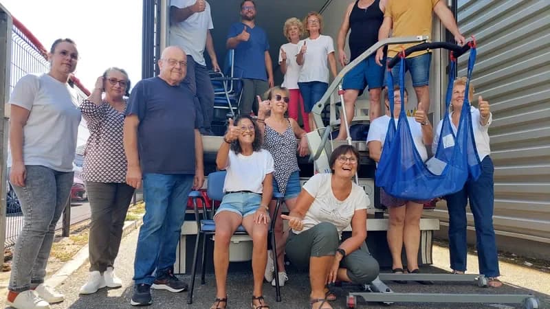 Une quinzaine de bénévoles posent, pouce levé, devant un camion chargé de fauteuils et de matériel médical.